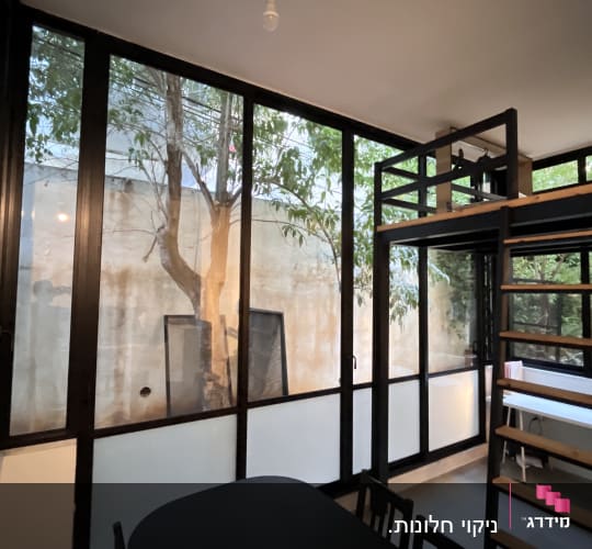 חלונות גדולים עם מסגרות שחורות, שולחן וכיסאות